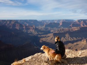 A photo of Jamie with a dog looking over a large canyon